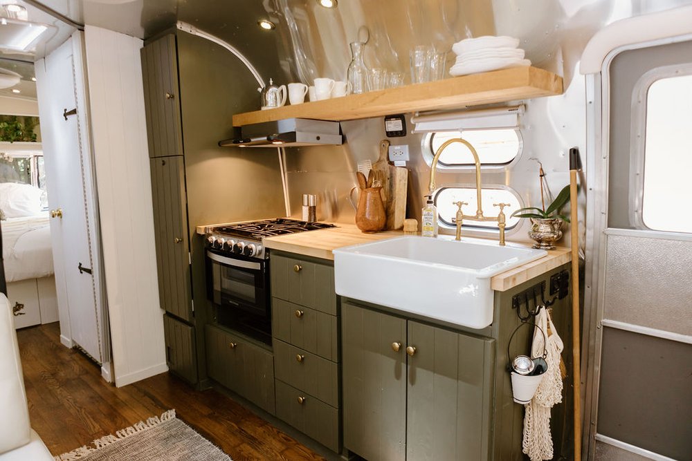 kitchen with dark green cabinets, brown, wooden shelves and countertop and a white sink