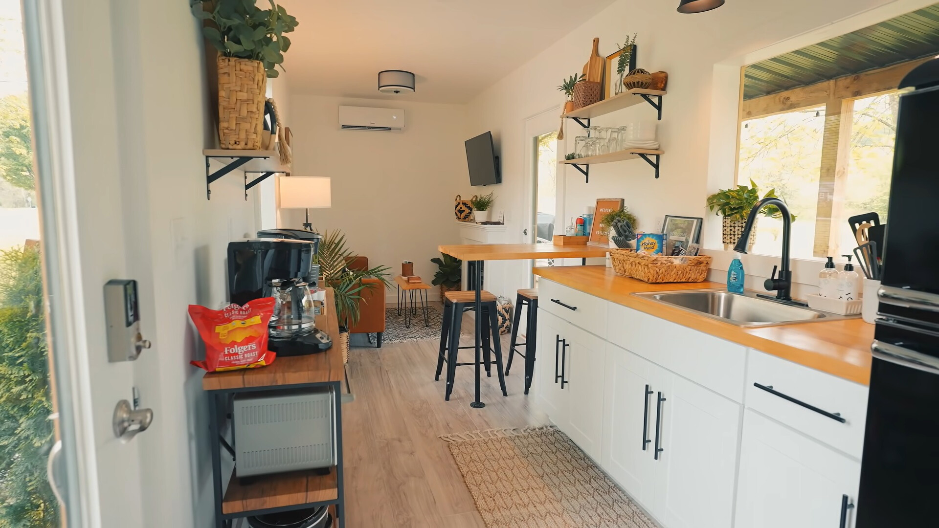 kitchen with white cabinets, brown countertop, windows on both sides, a built in dining table with two bar stools and an open brown shelf with kitchen supplies