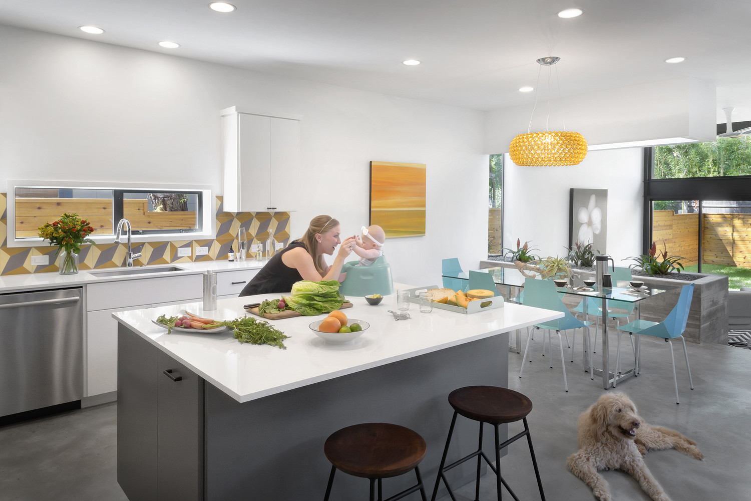 kitchen with a white countertop and cabinets, orange, beige and gray tiles, orange chandelier and an orange painting