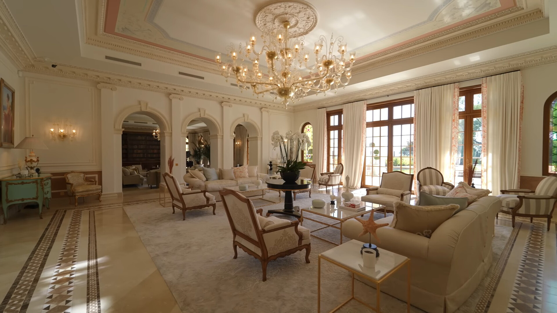 living room with white couches, glass tables, floor to ceiling windows, a big white chandelier