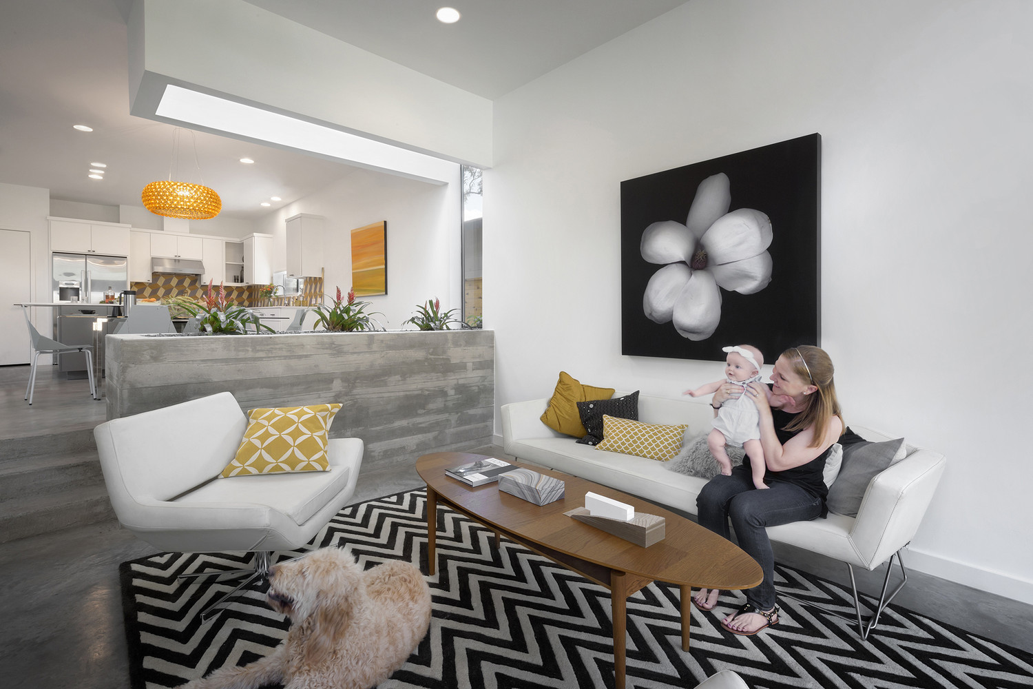 living room with a black and white flower painting on the wall, white couch and a cool white chair, oval brown table and a black and white carpet