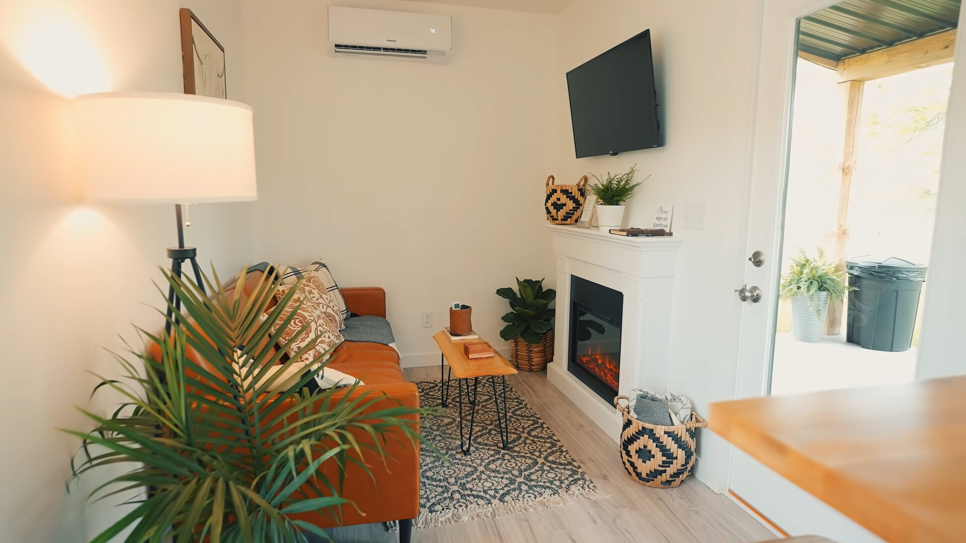 living room with an orange couch, a mini brown table, a flat screen tv and an electric fireplace and plants