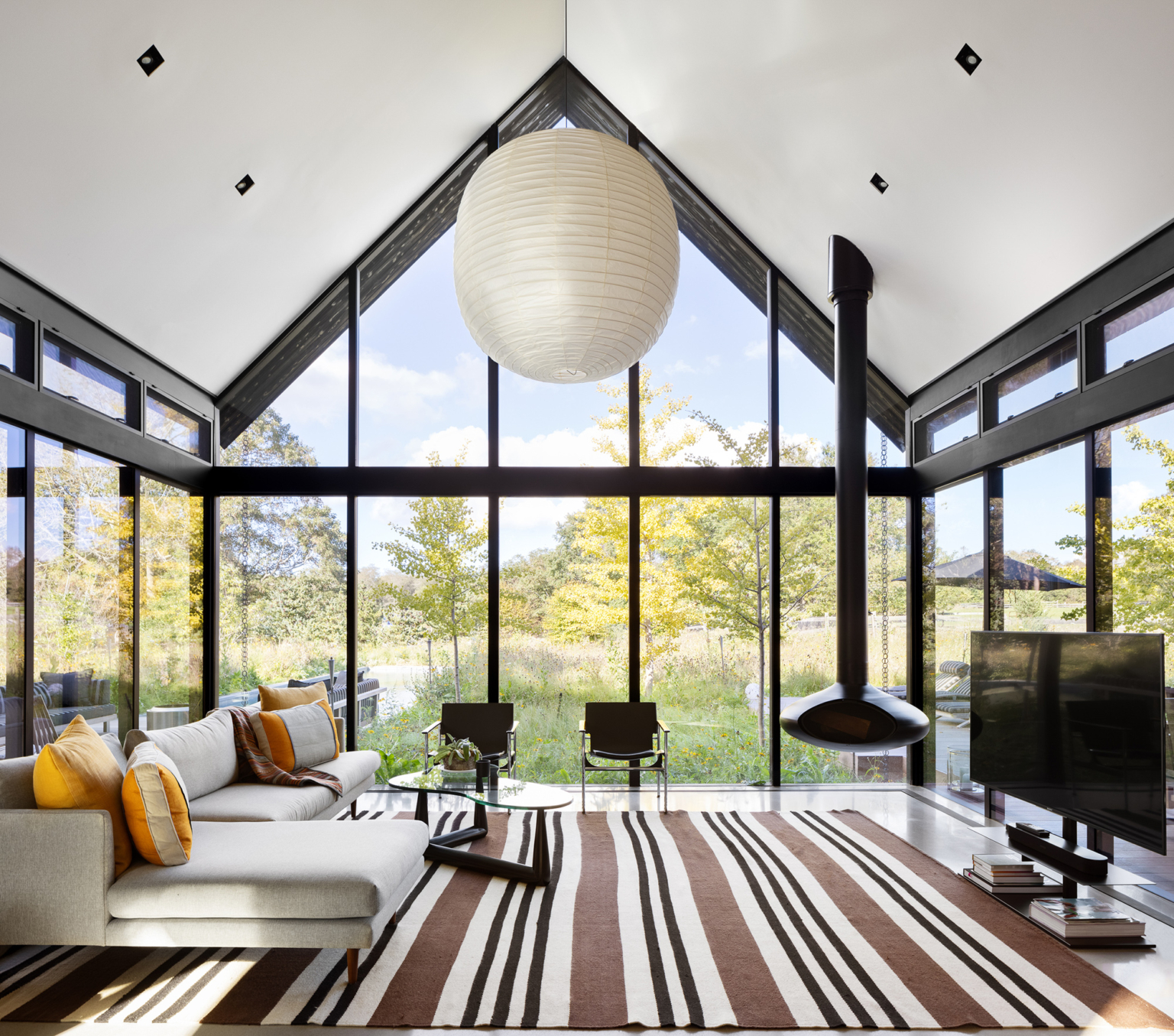 living room with floor to ceiling windows, flat screen tv, light gray l shaped couch and a glass table