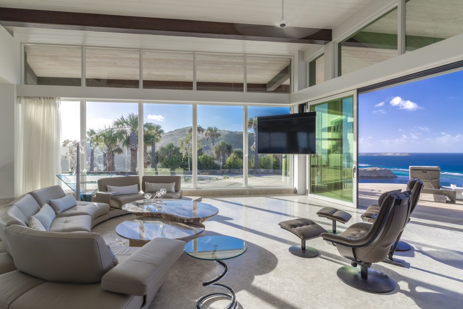 living room with a big white couch, flat screen tv and floor to ceiling windows with ocean view