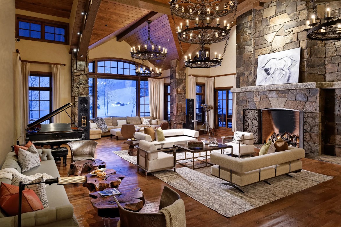 living room with a lot of white couches, huge windows, fireplace, candle chandeliers and wooden tables