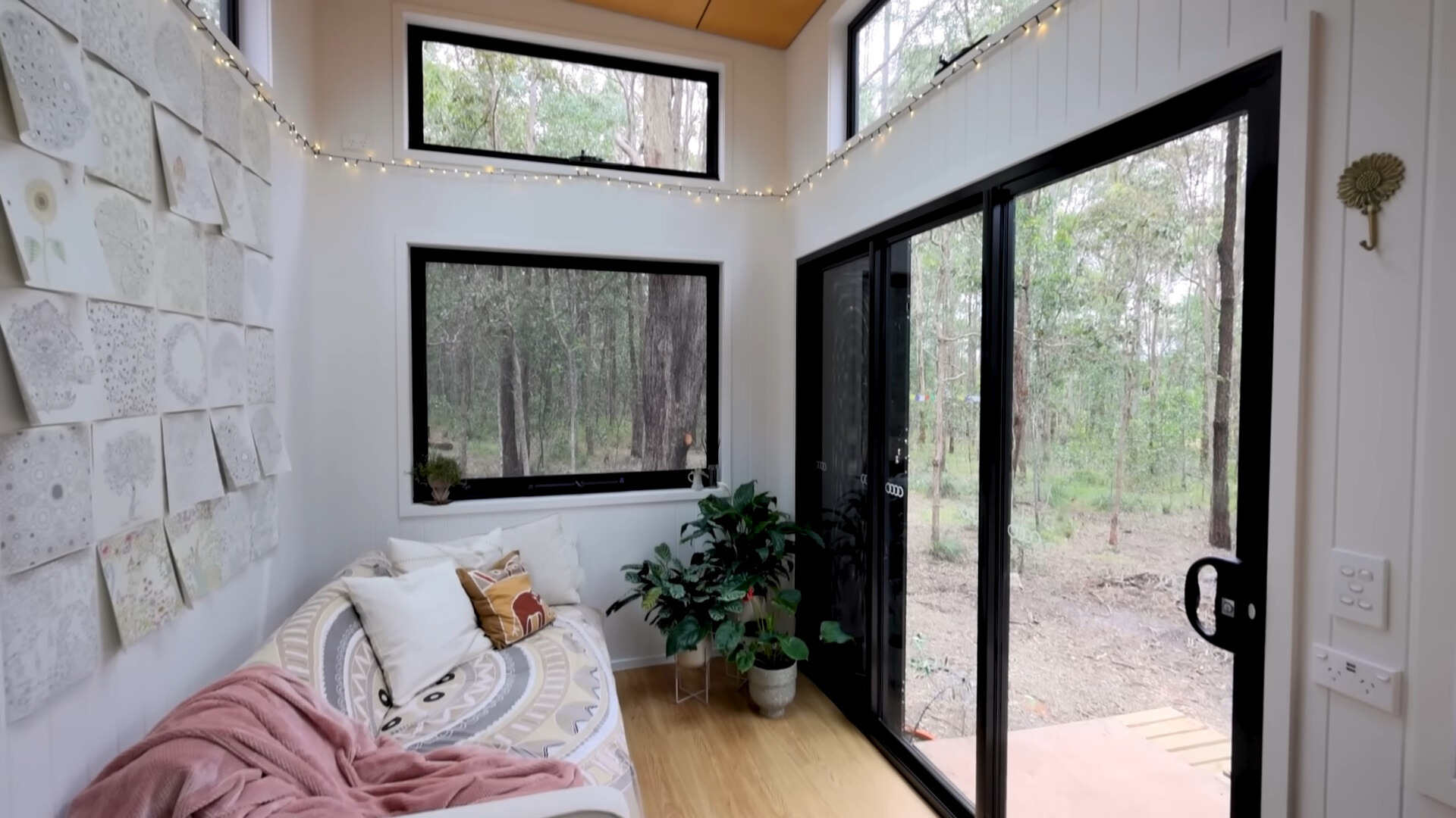 living room with many windows around, a comfy couch, a plant and coloring book pages on the wall