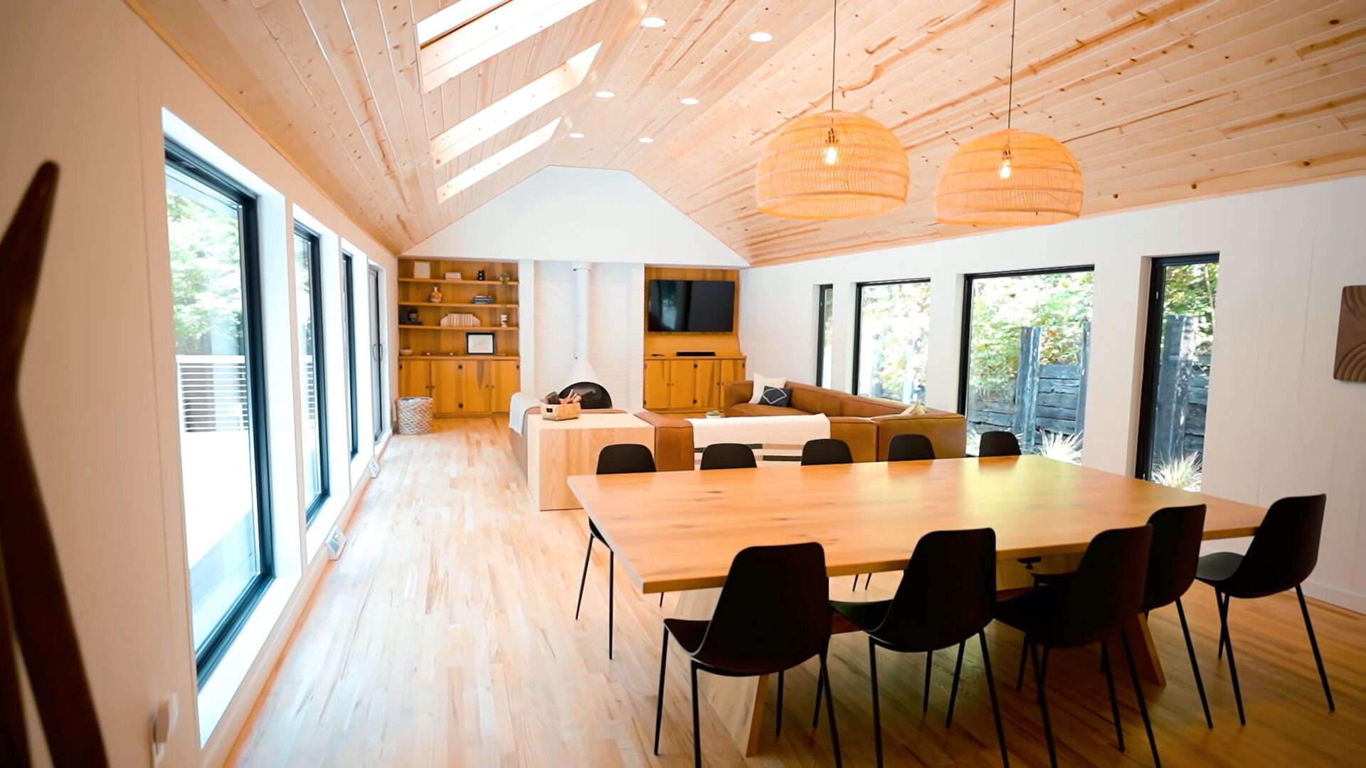 brown dining table with black chairs, brown couch, windows on both sides of the house and ceiling windows, flat screen tv