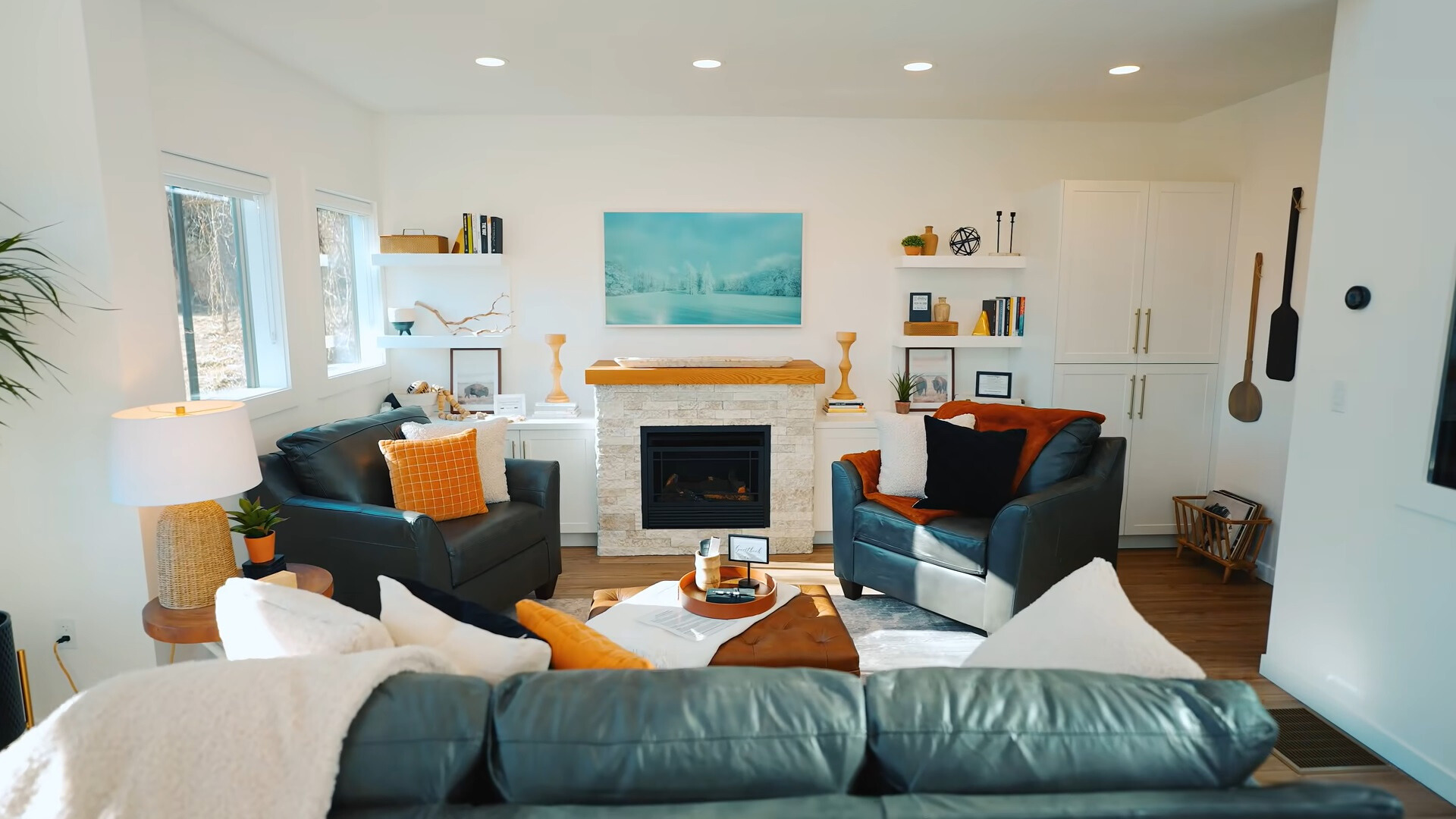 living room with black leather couches, brown table, white shelves with decor and white cabinet