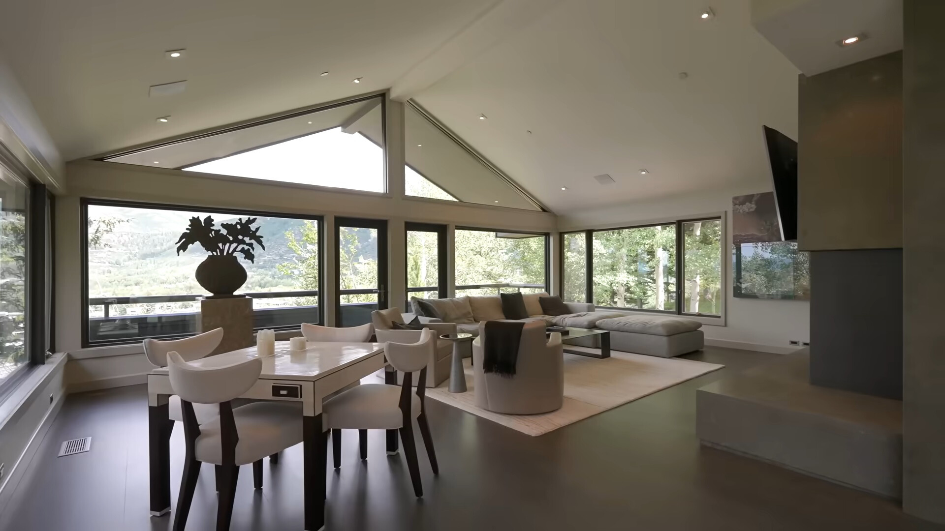 living room with an l-shaped couch, big windows and a small white table surrounded by white chairs