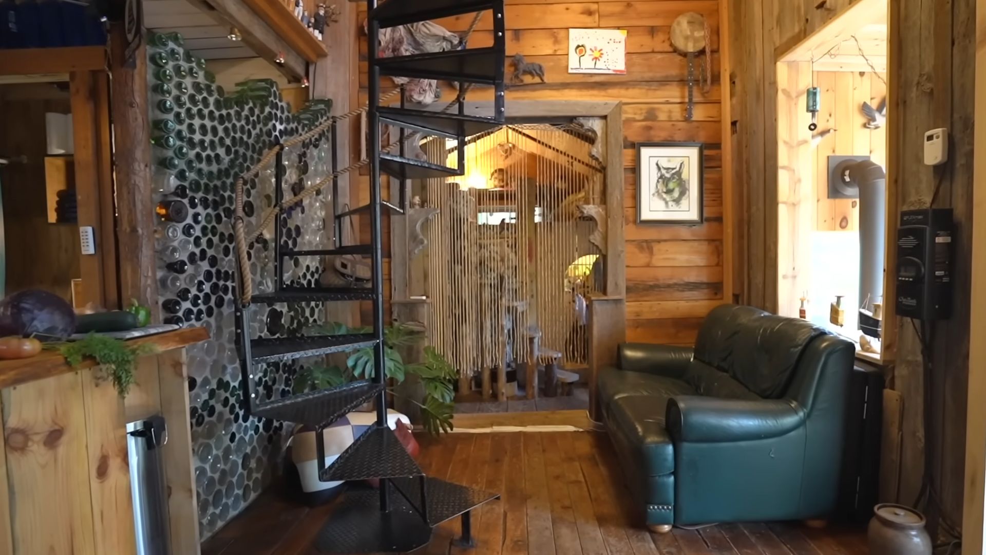 small libing room area with a black leather couch, spiral stairs right next to it, wooden walls and floors