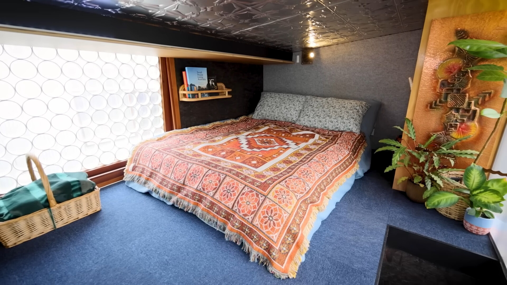 loft bedroom with a big bed, textured sheets, brown shelf, brown closet and a window with round shades