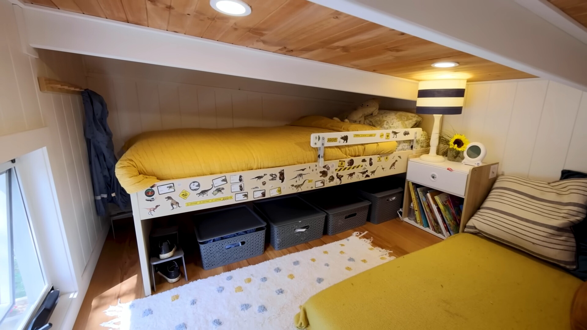 loft bedroom with a bed with yellow bed sheets and a bedside table with books and storage baskets under the bed