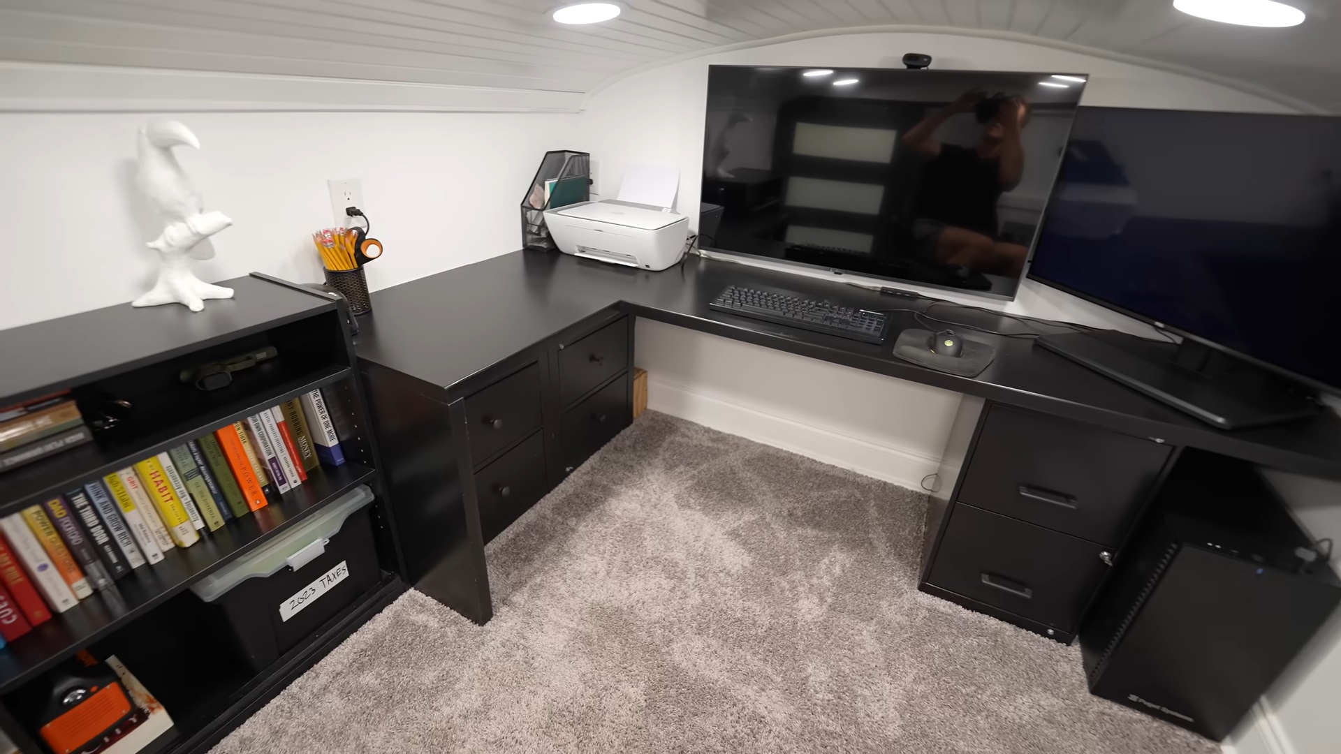 office area of a tiny home with a black desk, two monitors, a black cabinet and a printer