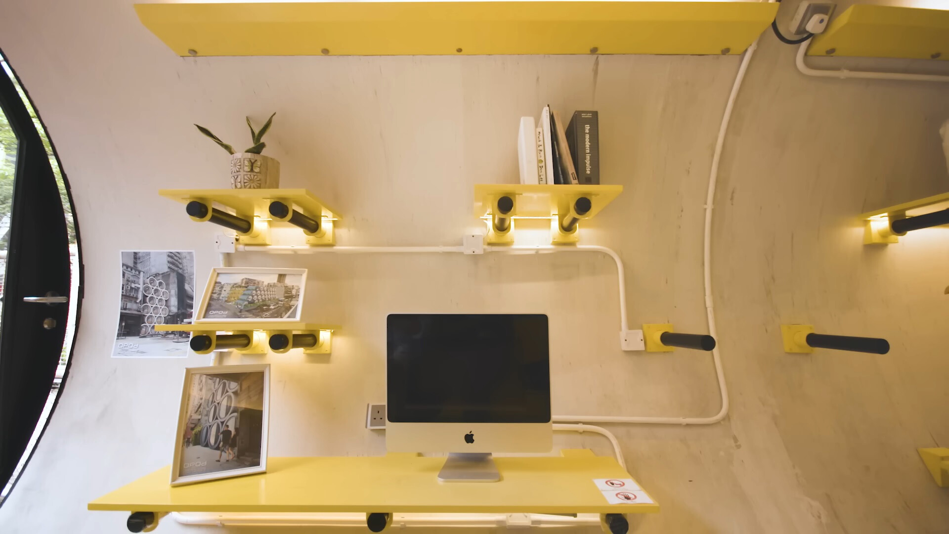 office area with a desk, computer, shelves above the desk with books, photos and potted plant