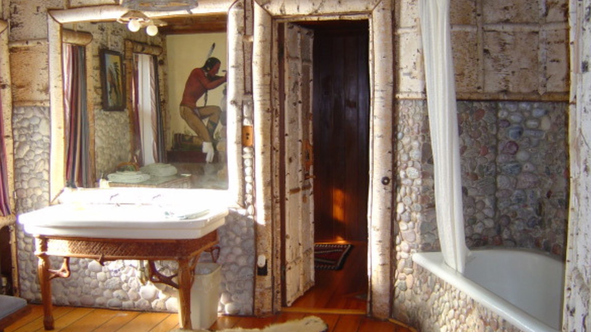 one of the bathrooms in the granot loma with birch wood walls and accents and stone details, a white bear rug on the floor, and an old mirror with a vanity