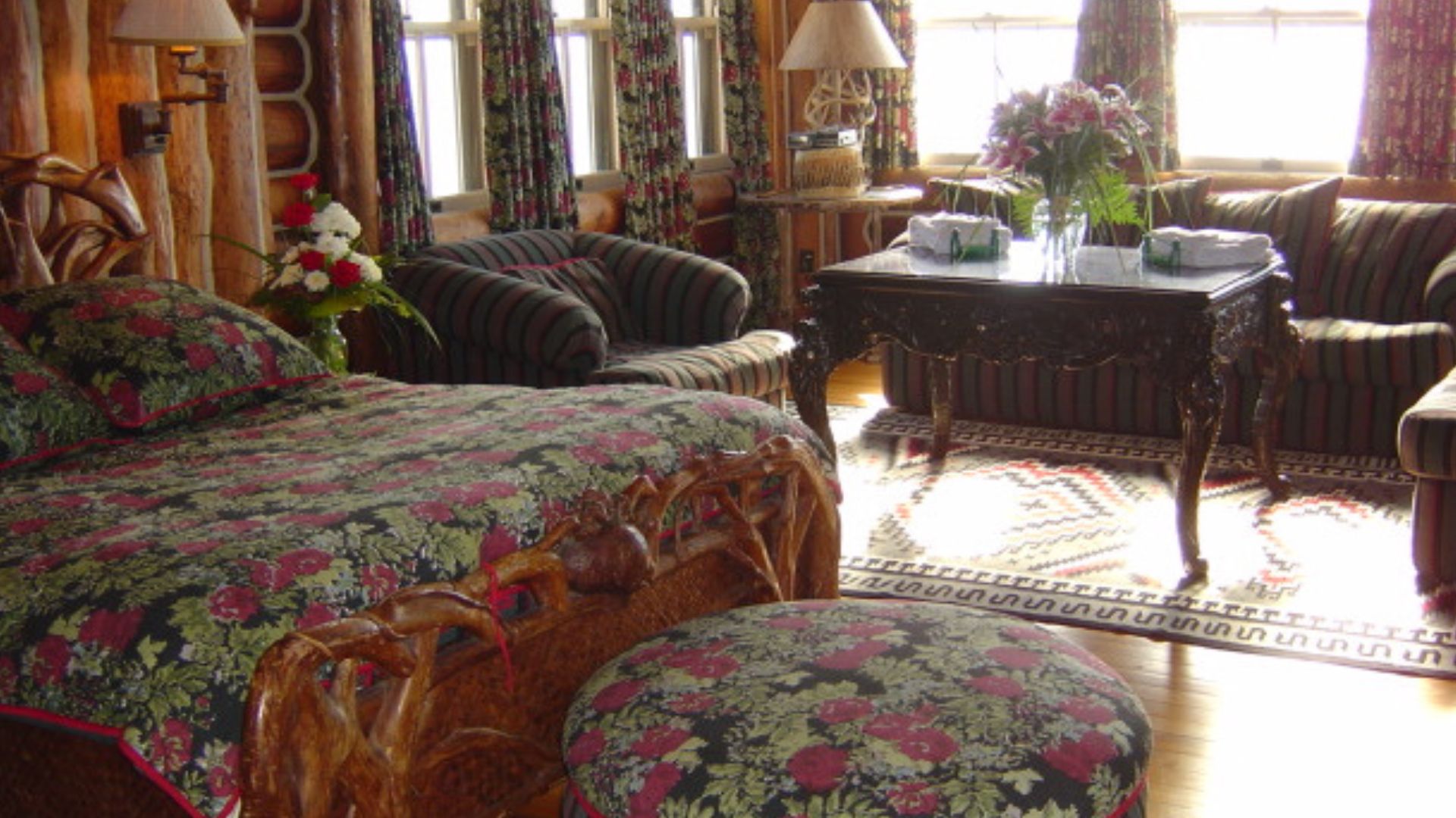 a bedroom in granot loma, featuring rustic wooden furniture, floral-patterned bedding and curtains, and a cozy seating area with striped upholstery