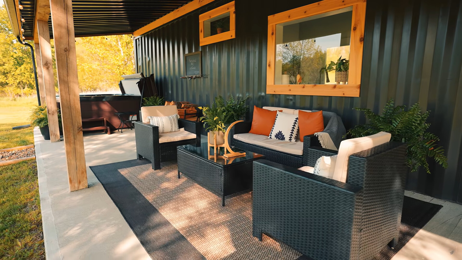 outside area of a container house with a cushioned black couch and sofas, a black table and a hot tub