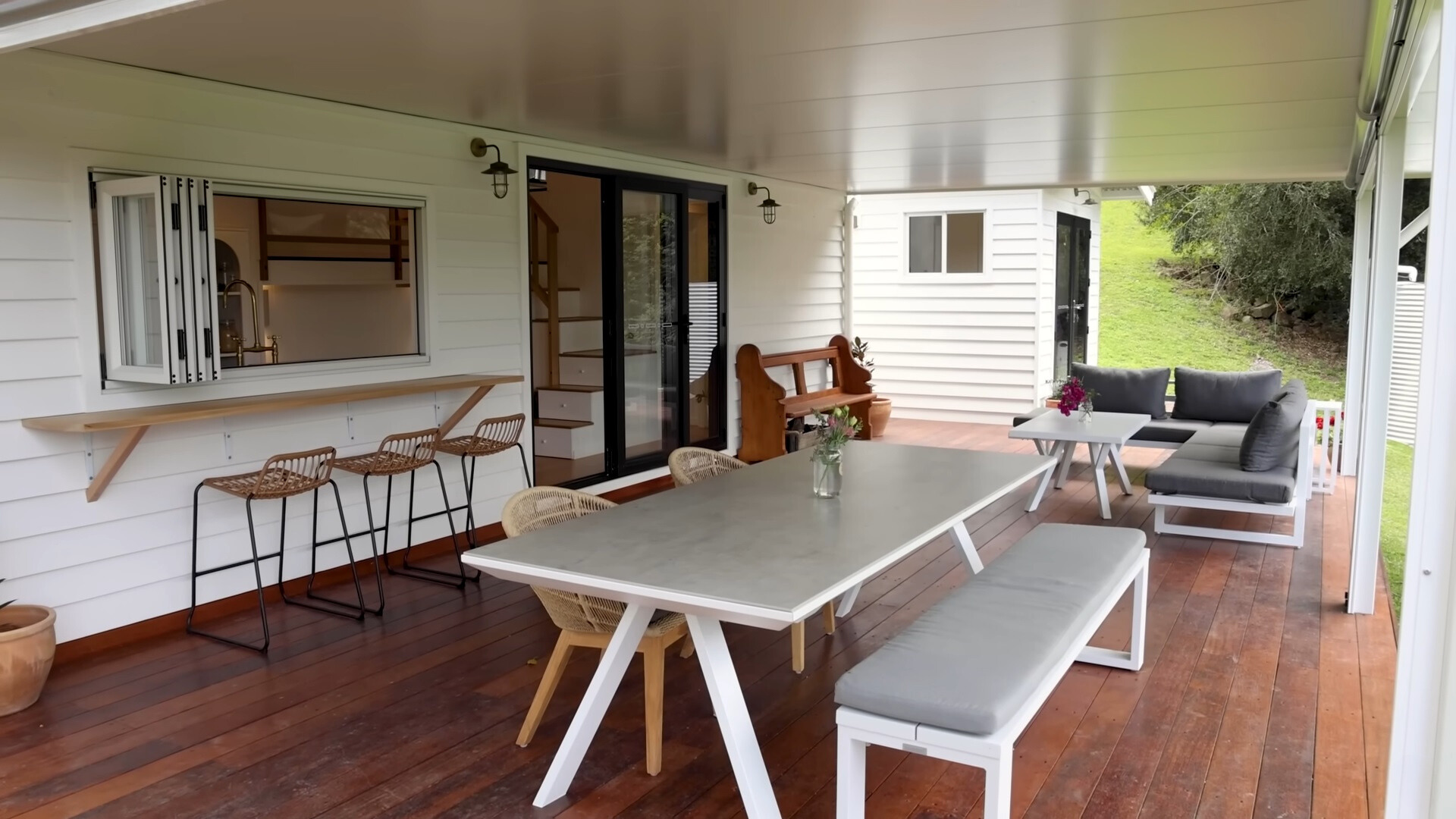 outside area with a big, white dining table, cushioned sitting area with a white table and a built in table with bar stools