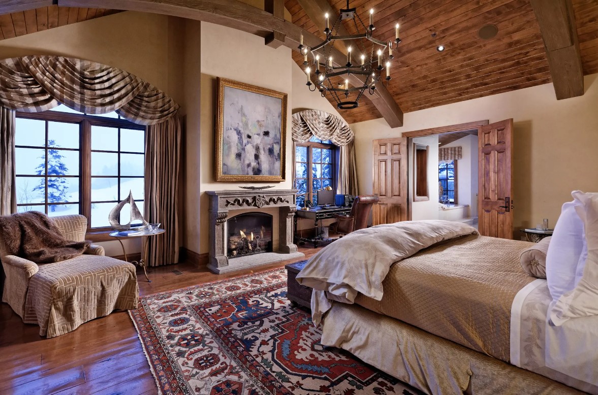 primary bedroom with a big bed, candle chandelier, fireplace, sofa in the corner and big windows