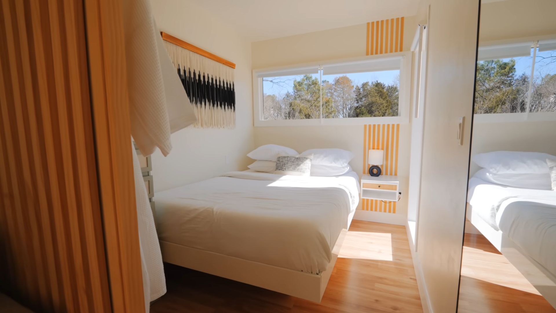 small bedroom with a queen bed in the corner, floating bed and floating nightstand, big windows on to walls, light color palette used