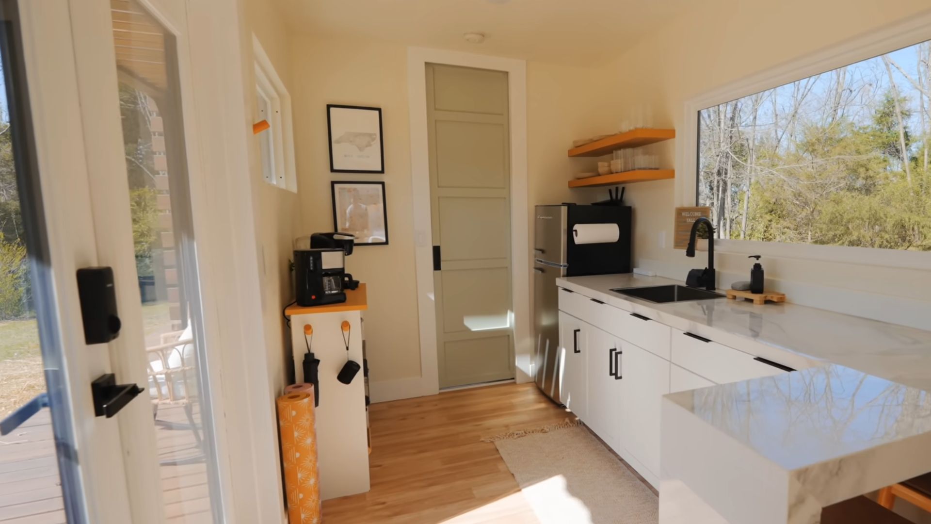 small kitchenette on one end of the container, white marble countertops, a dining area in the corner, a big window on the right, and a bathroom door in the back