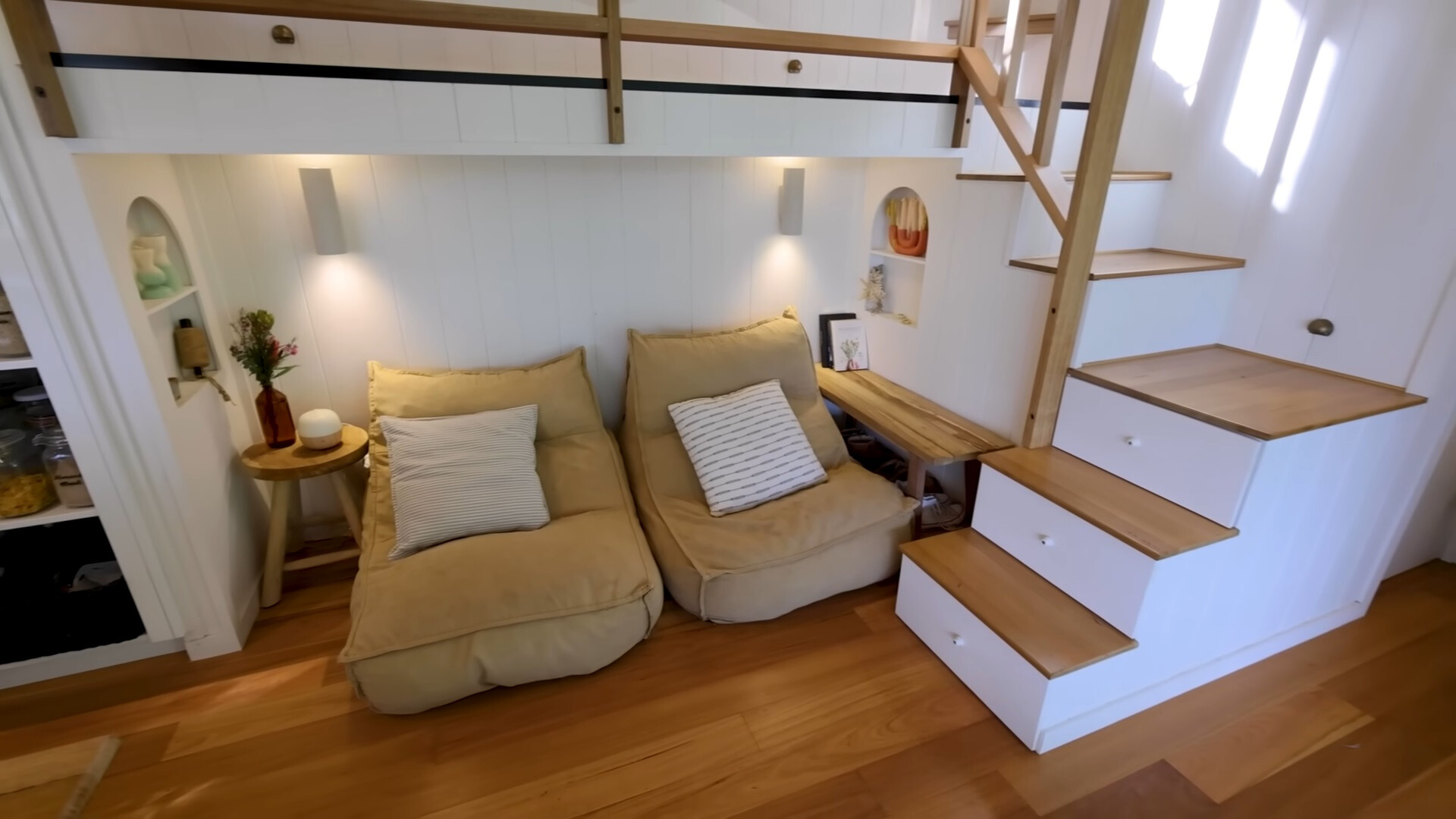 hangout area with two tiny beige sofas and stairs which hide storage inside