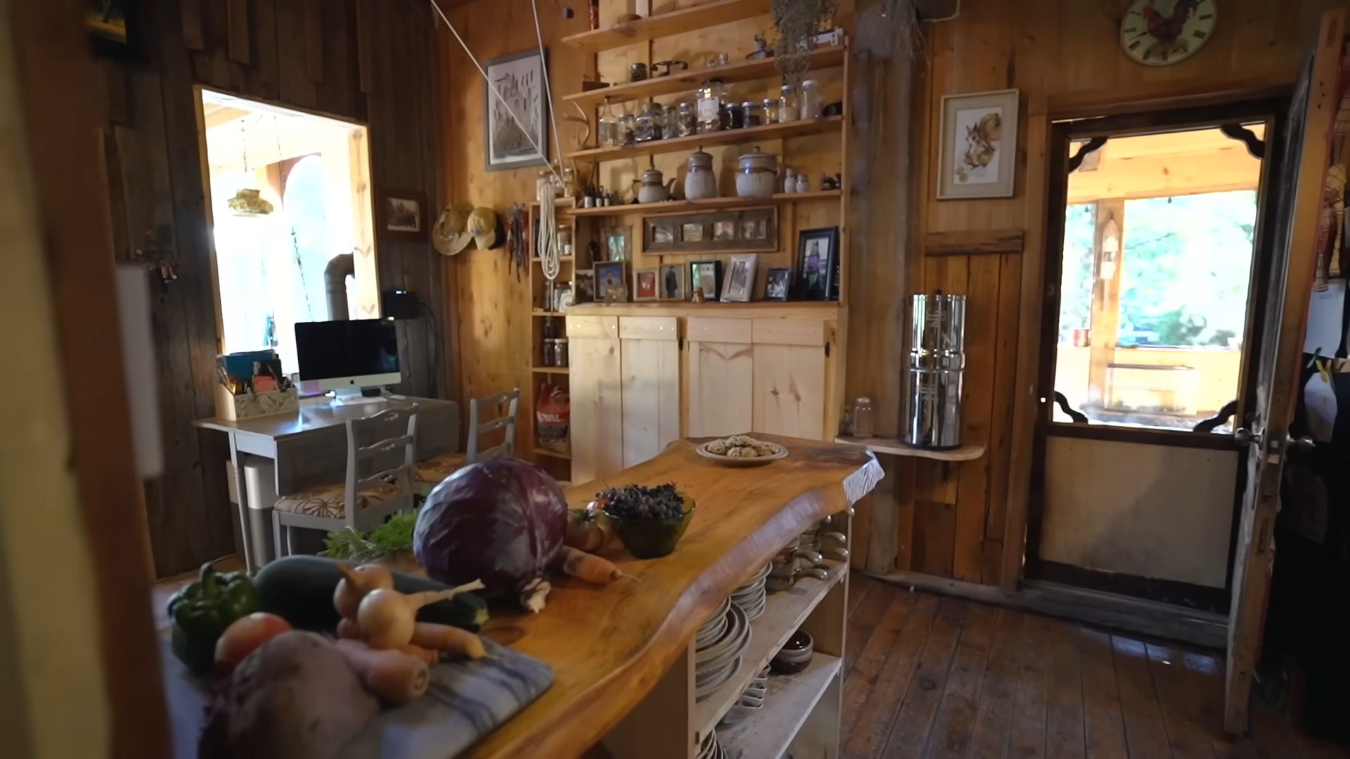 view from the kitchen into a small office with a computer, a dresser with shelves next the screen door on the right