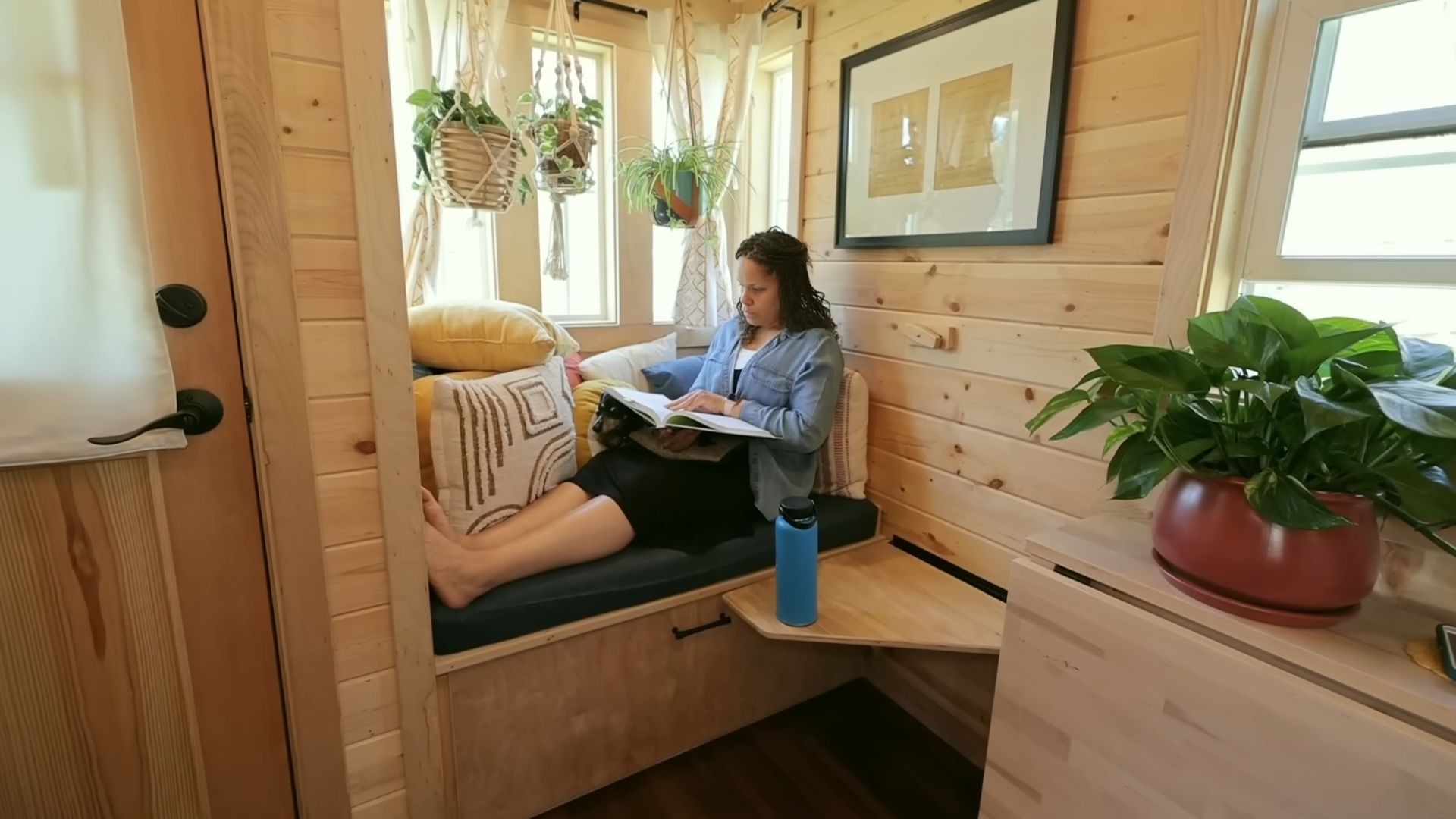 woman named Denetra sitting and reading a book in her tiny living room nook, a side table on her right