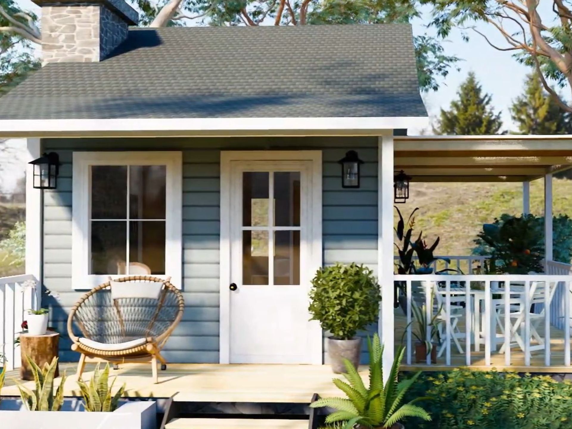 exterior of the dainty house with grey roof and blueish grey facade, front porch with a round chair next to the front door, side porch with white picket fence and a seating area, lots of plants and flowers around the house