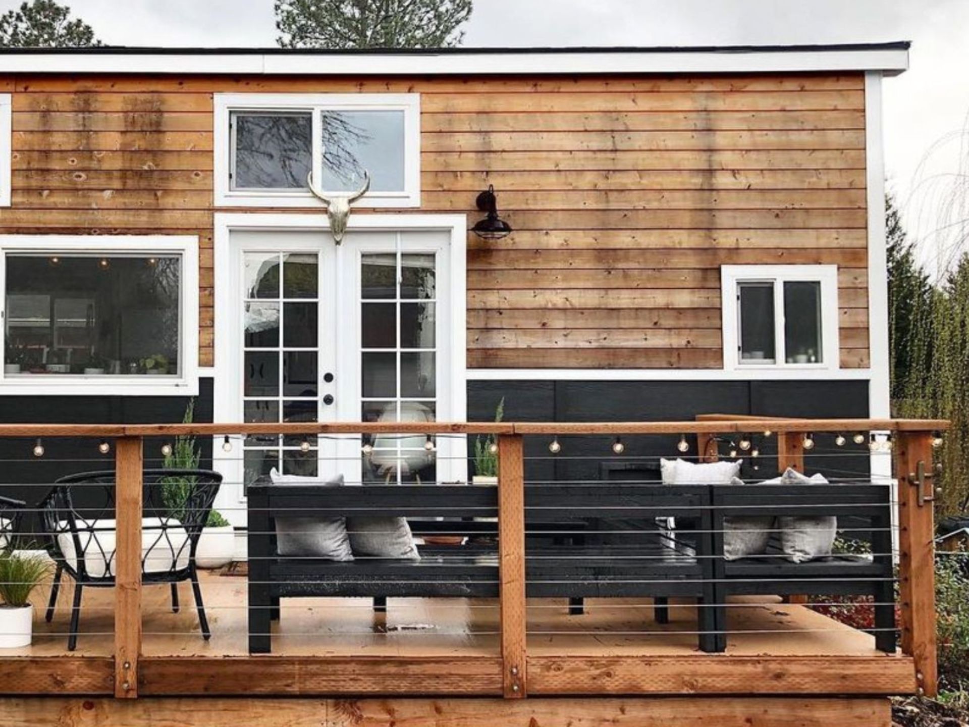 exterior of the THOW with wood siding, windows and french doors in white, a small patio with black furniture by the entrance