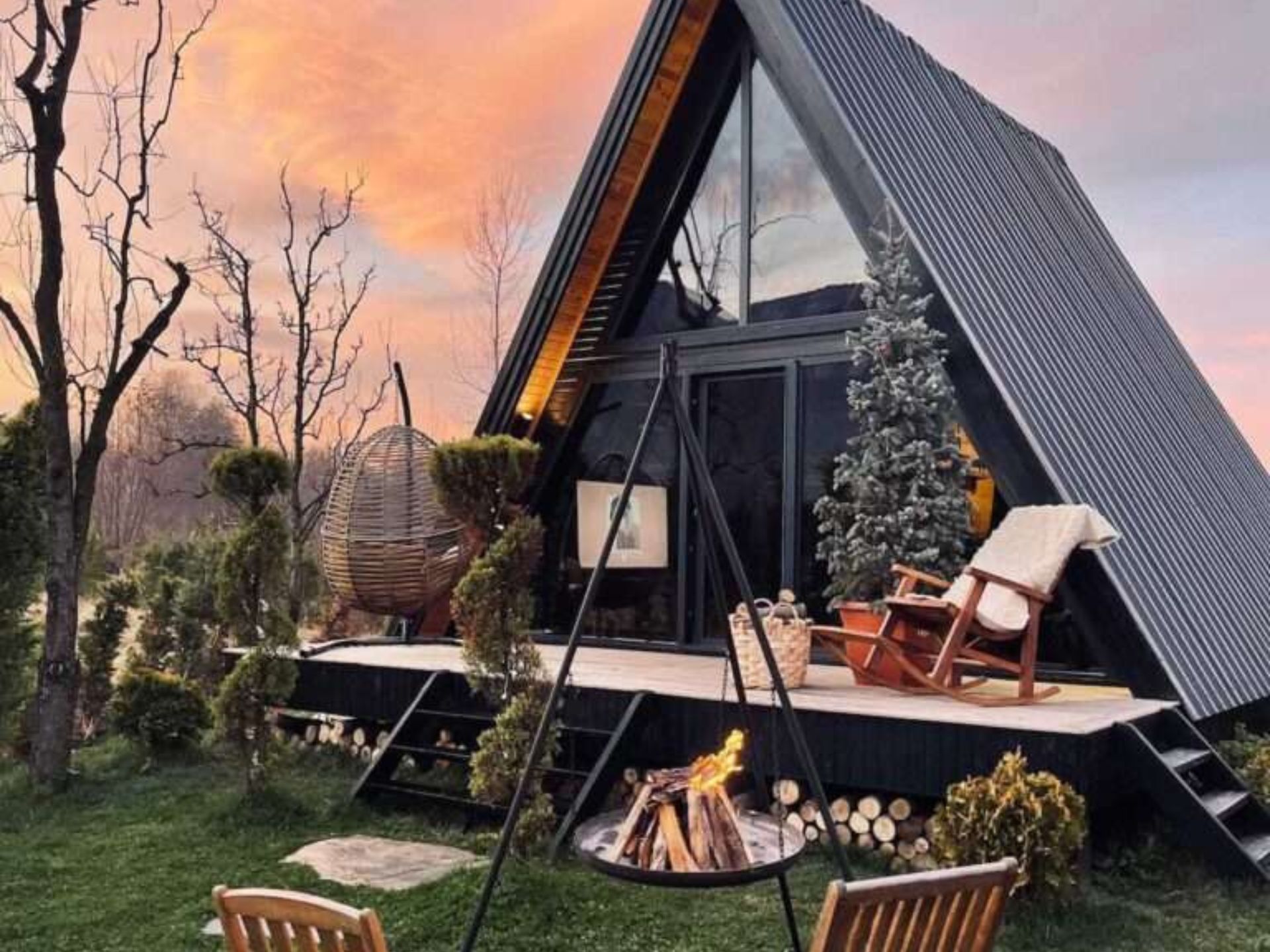 side photo of the A-frame bungalow perla in winter time with a fire pit visible, Christmas tree on the front porch, rocking chairs and some lounge chairs as well