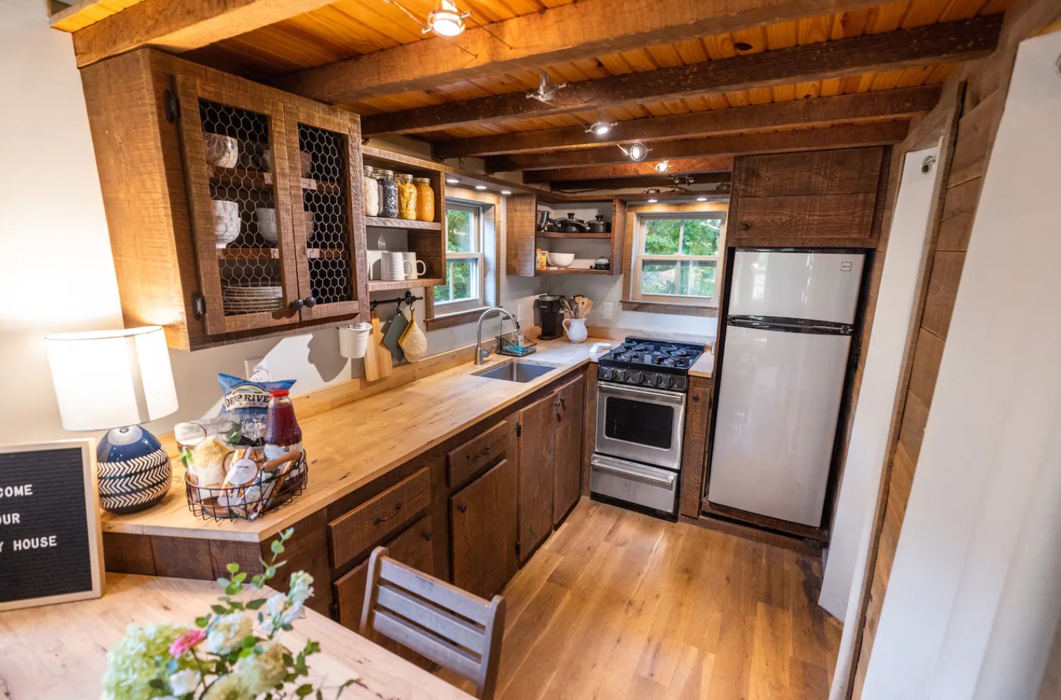 Tiny wooden kitchen with exposed shelves and elevated fridge