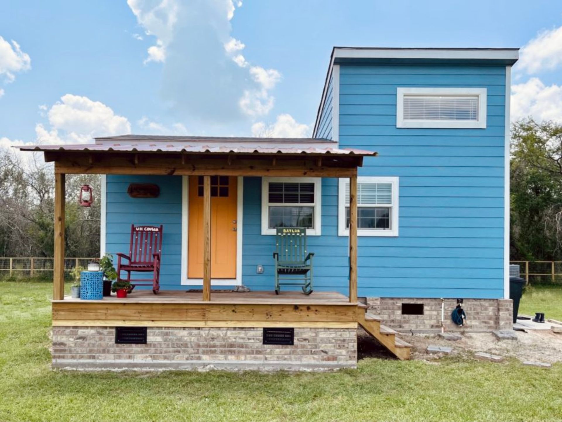 exterior of a tiny house with a blue wall and a mini porch with two rocking chairs