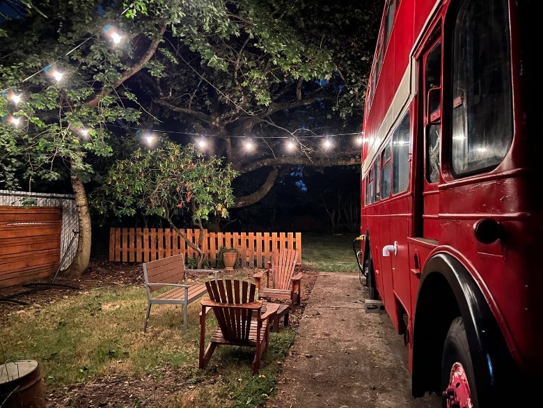 backyard of a double decker bus home with a bench and two chairs and string lights