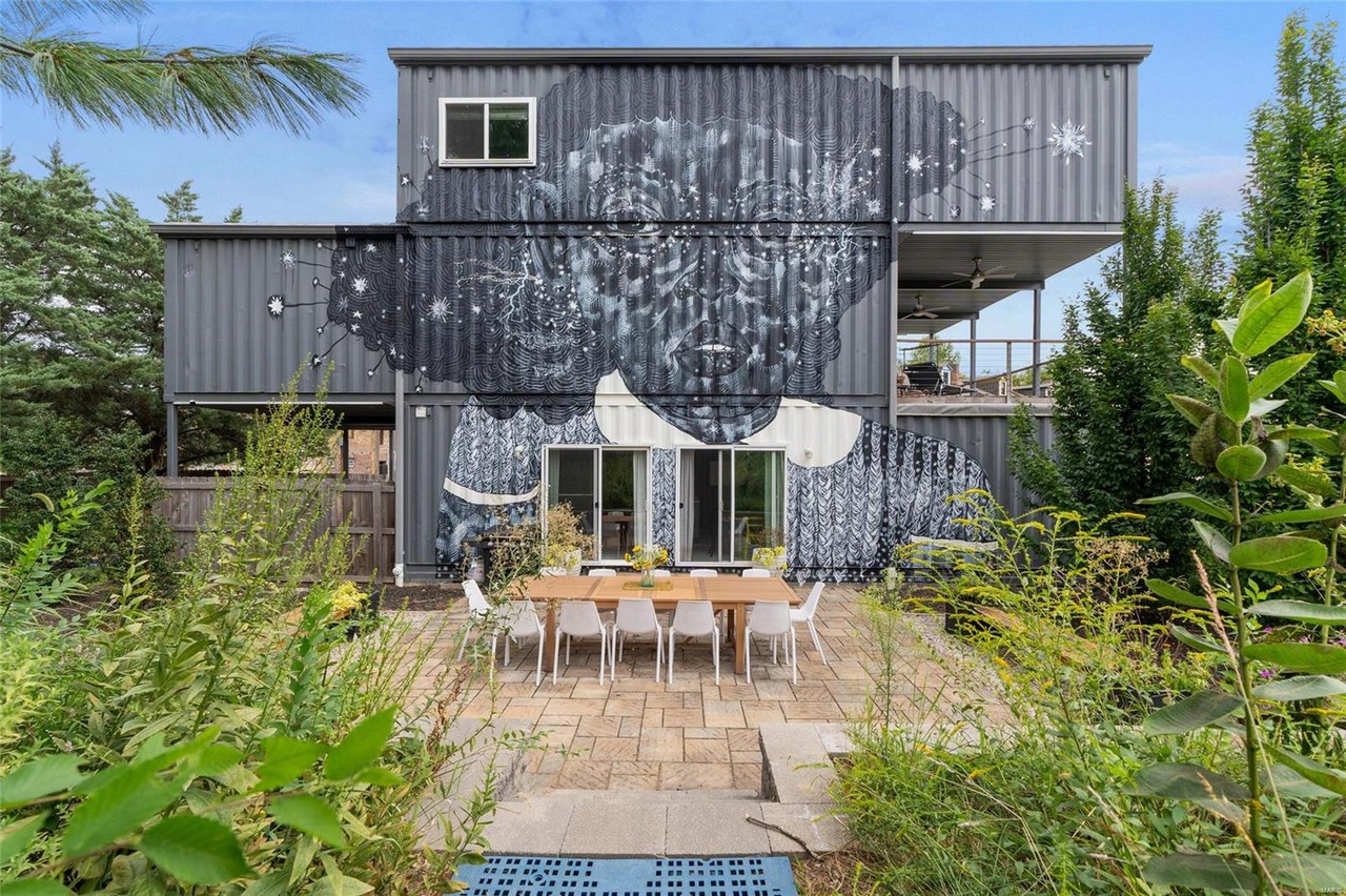 backyard of a container home with a gray mural and a dining table accompanied by white chairs