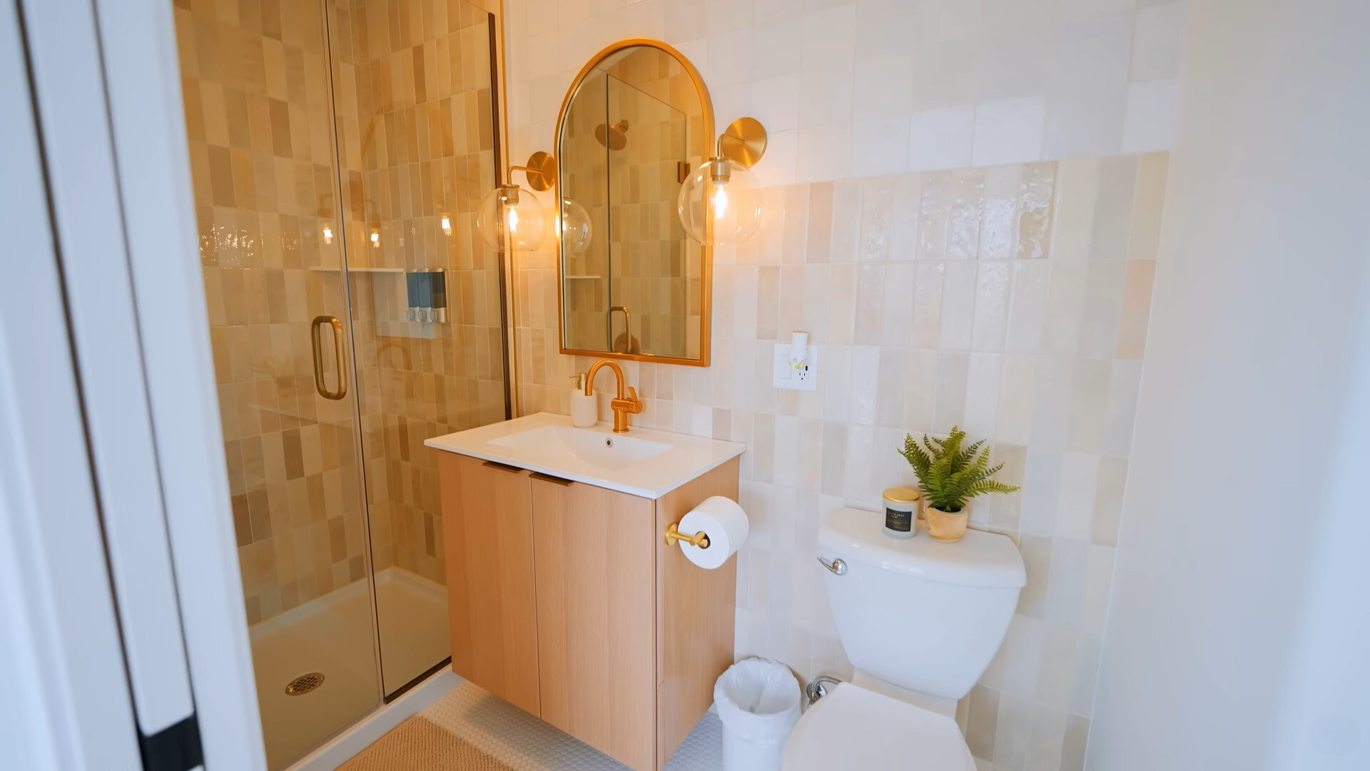 bathroom with a glass shower, light beige tiles, white sink and brown cabinet and warm lightning