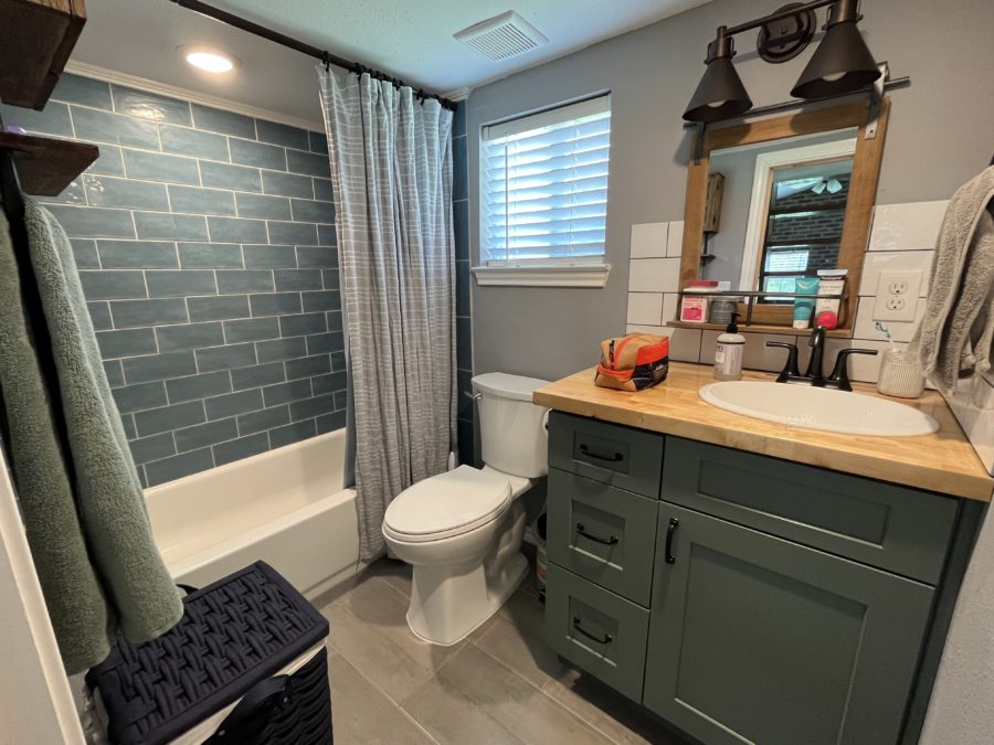 bathroom with a green cabinet and brown countertop, white bathtub and green tiles