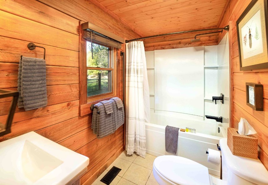 bathroom with wooden walls, white bathtub, white sink and a toilet