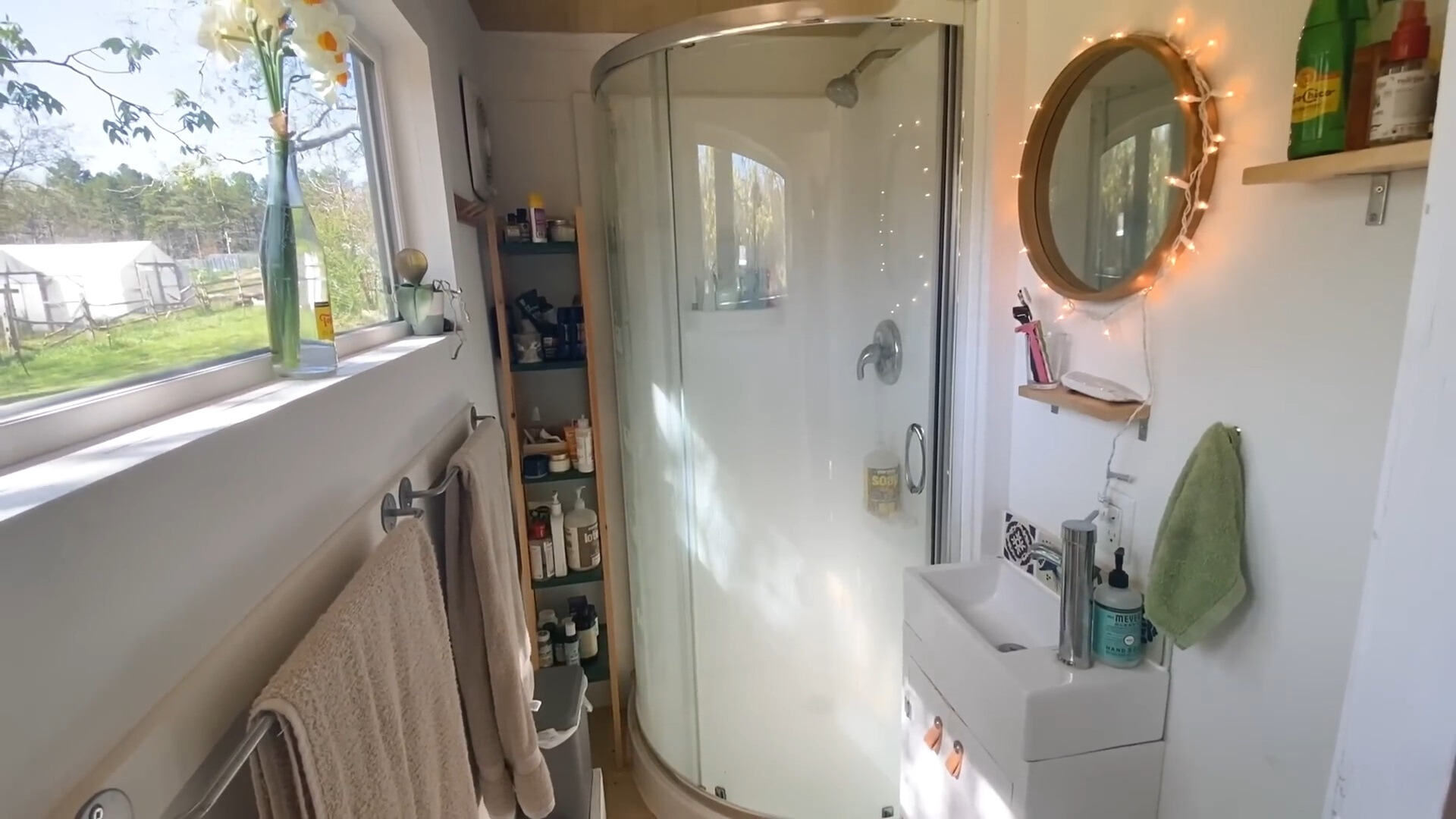 bathroom with a glass shower, tiny white sink with a white cabinet and a brown shelf in the corner