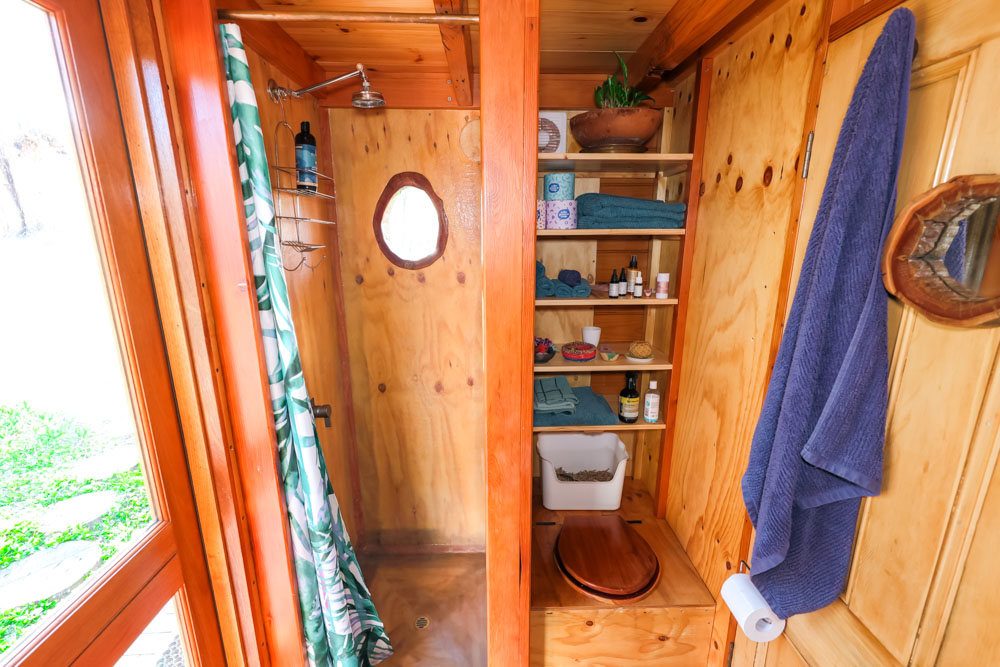 bathroom with wooden walls, small round window carved from a tree in the shower, open shelves