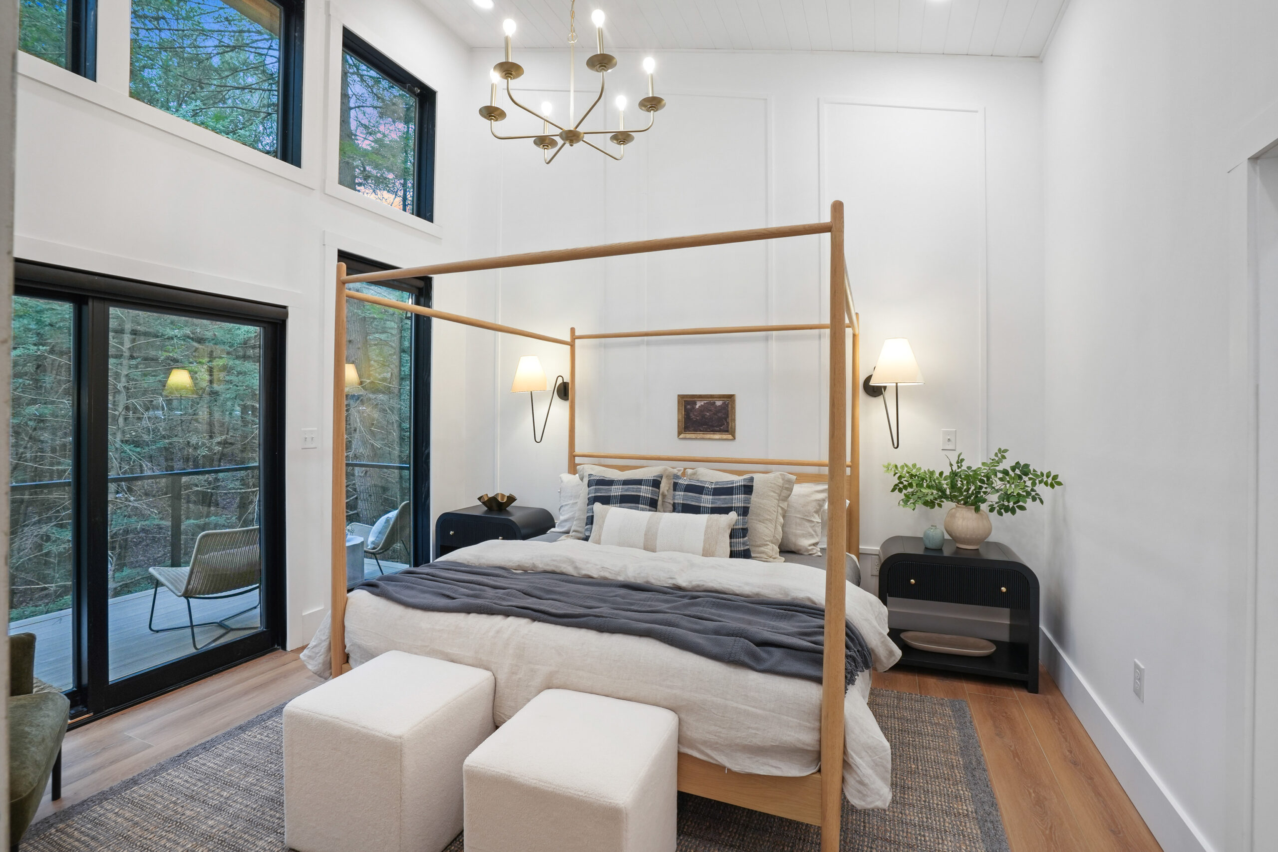 bedroom with a canopy king sized bed, black bedside tables with lamps above, opening to a deck