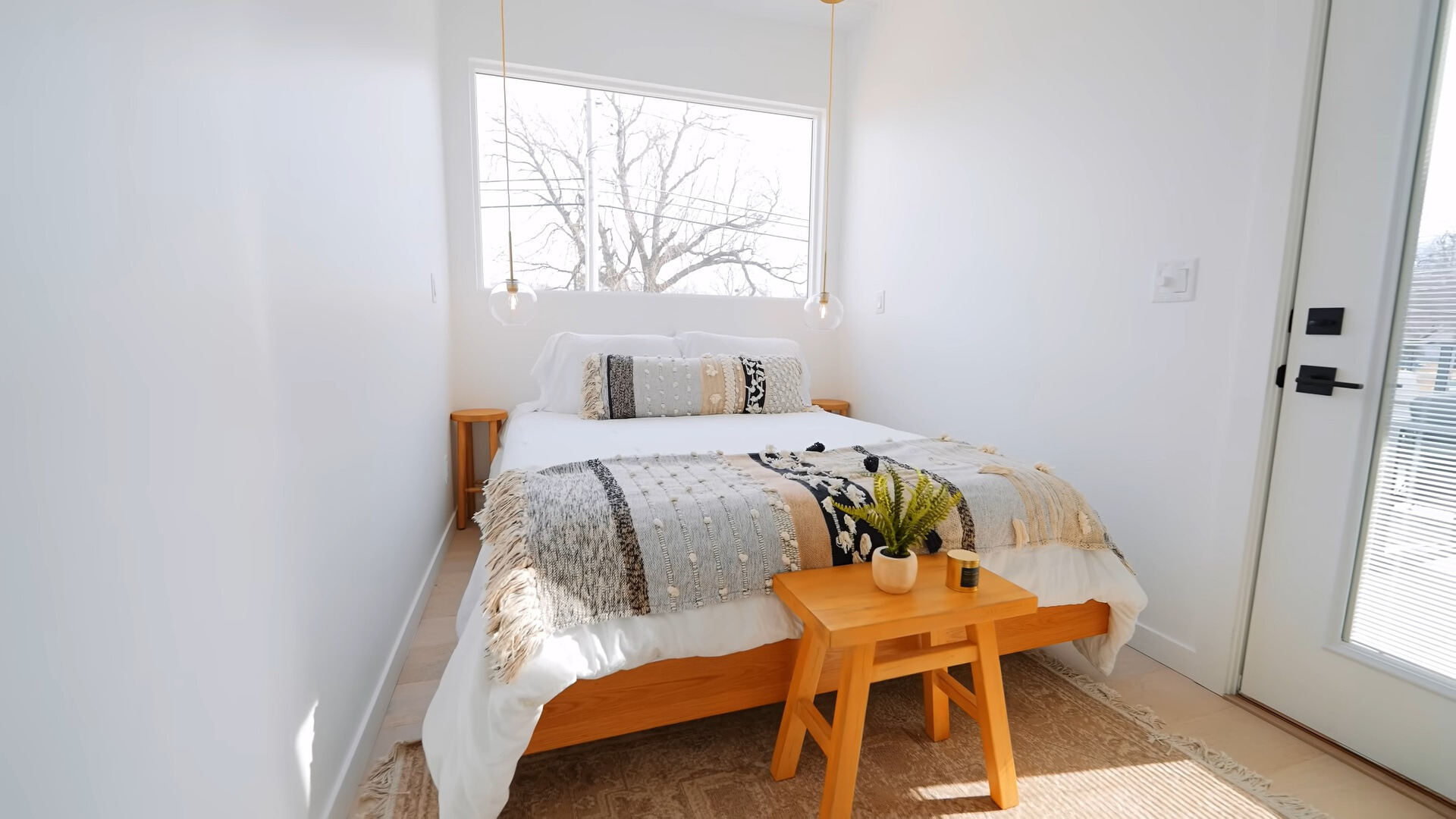 bedroom with a big bed, tiny round bedside tables with a window above and a mini brown table at the end of the bed