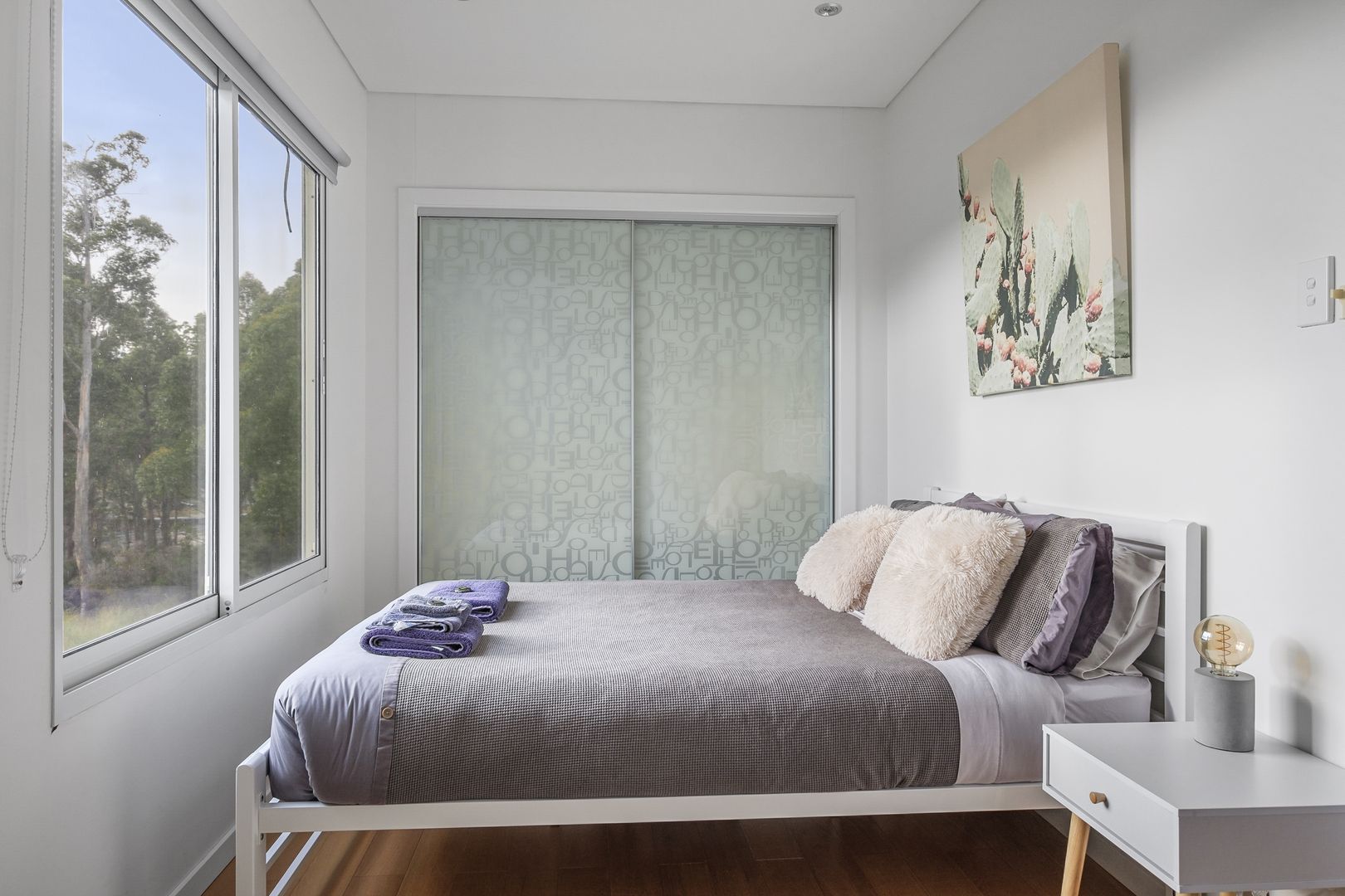 bedroom with one bed and white bedside table and a window opposite it