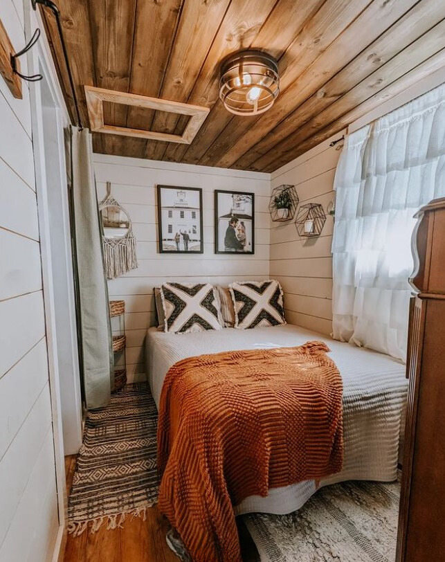 bedroom with white wooden walls and brown wooden ceiling and a comfy bed with photos hanging above the bed and shelves hanging on the wall