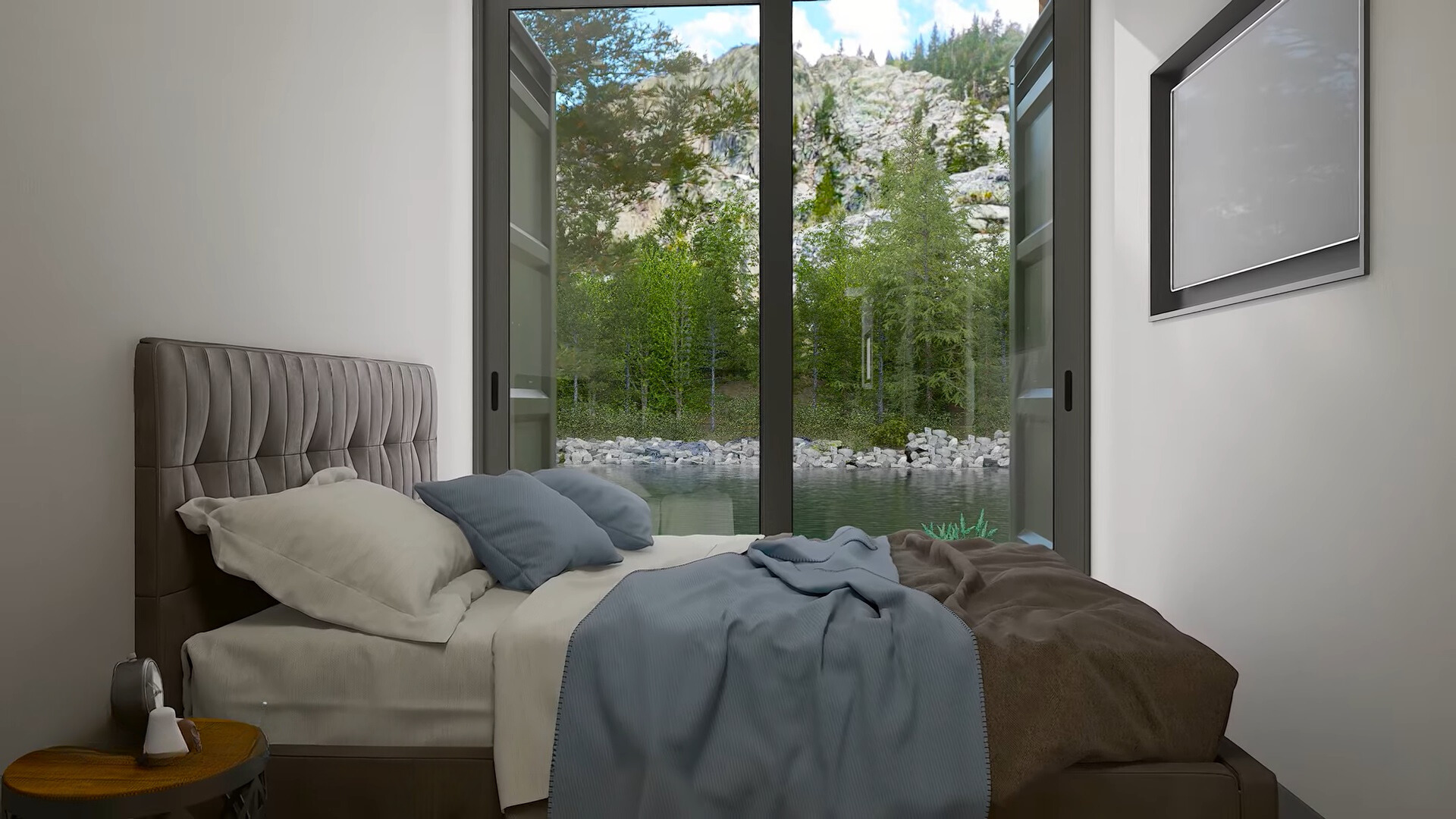 bedroom with a bed, bedside table, flat screen tv opposite the bed and a floor to ceiling window with a view of the river and trees