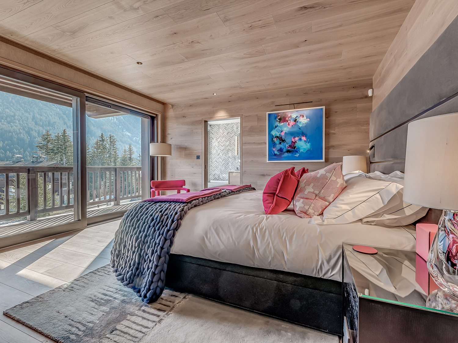 bedroom with a floor to ceiling window, big bed, pink chair in the corner and a bedside table