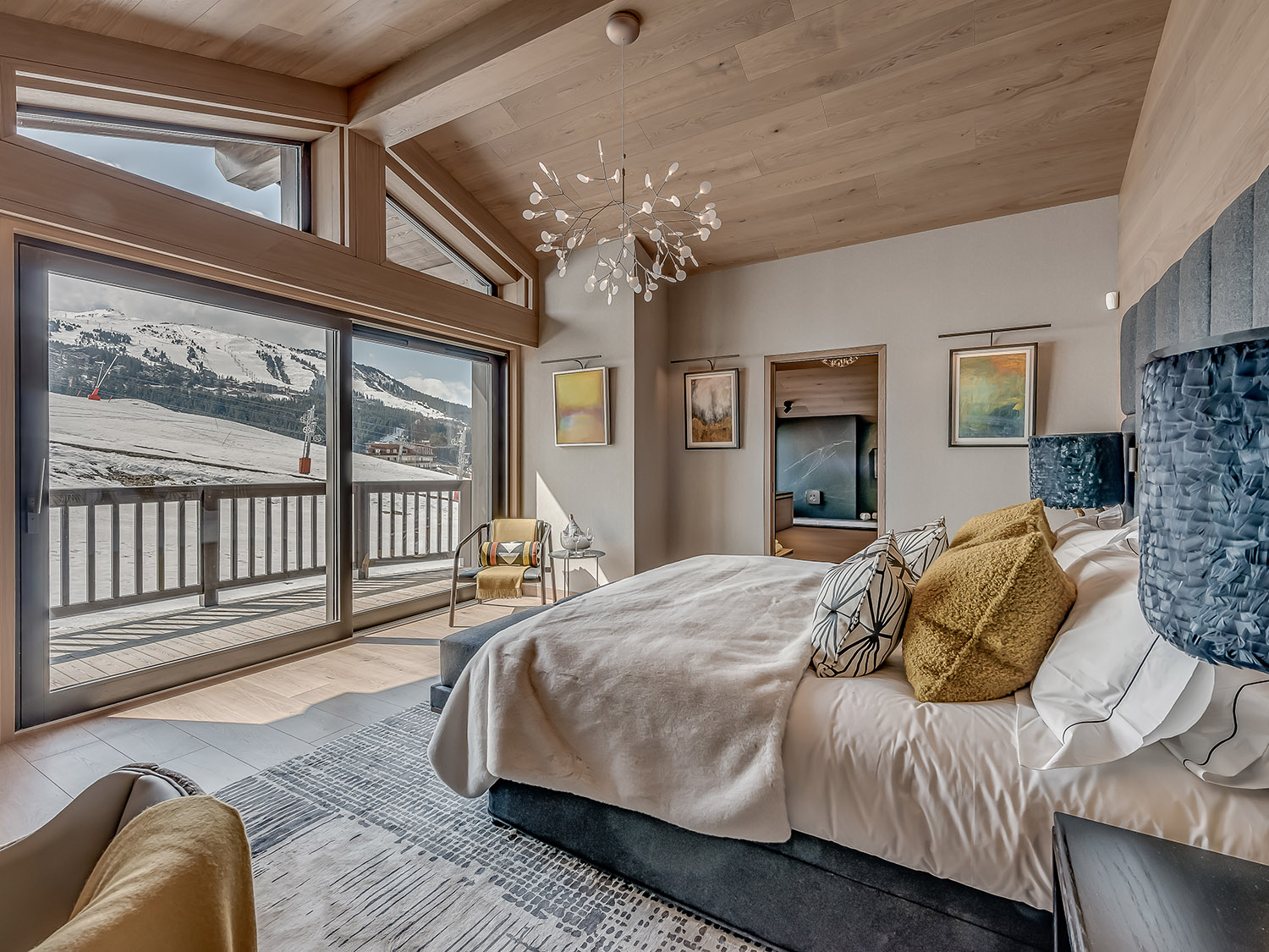 bedroom with a big bed, floor to ceiling windows, a chair in the corner, art pieces on the wall