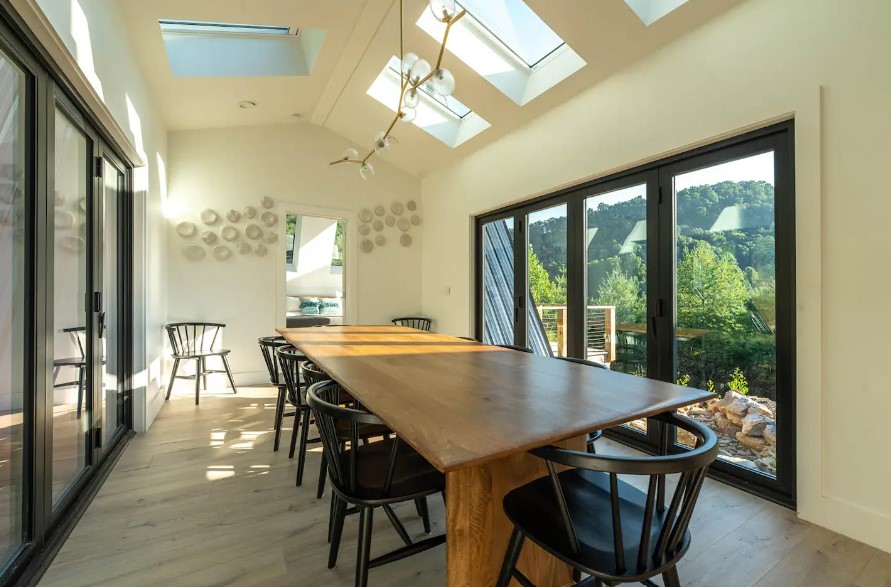 dining room with a long, brown dining table and black chairs and big windows on both sides