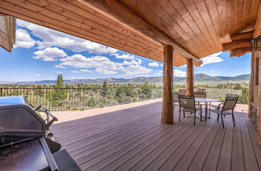 deck with a table and chairs and a silver grill and nature in the background