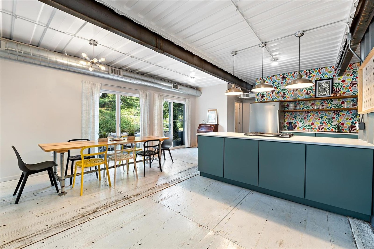 dining and cooking area with a long, brown dining table accompanied by black, white and yellow chairs, teal cabinets and white countertop